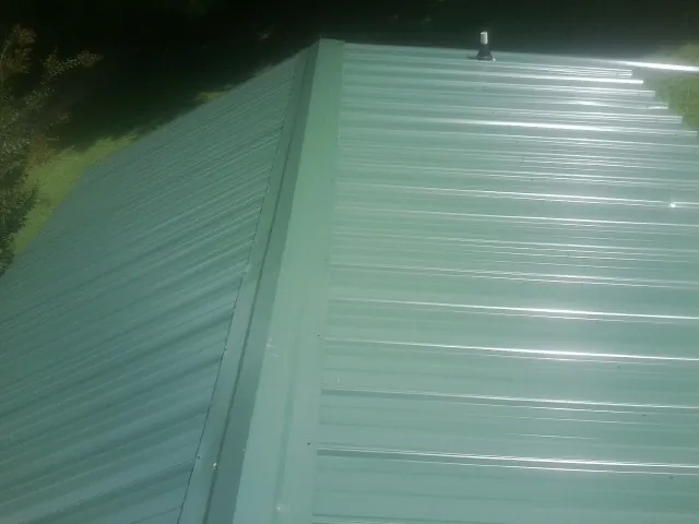New green metal panels meeting at the ridge of a roof — Flat Roof Repair work by our crew in Glen Gardner