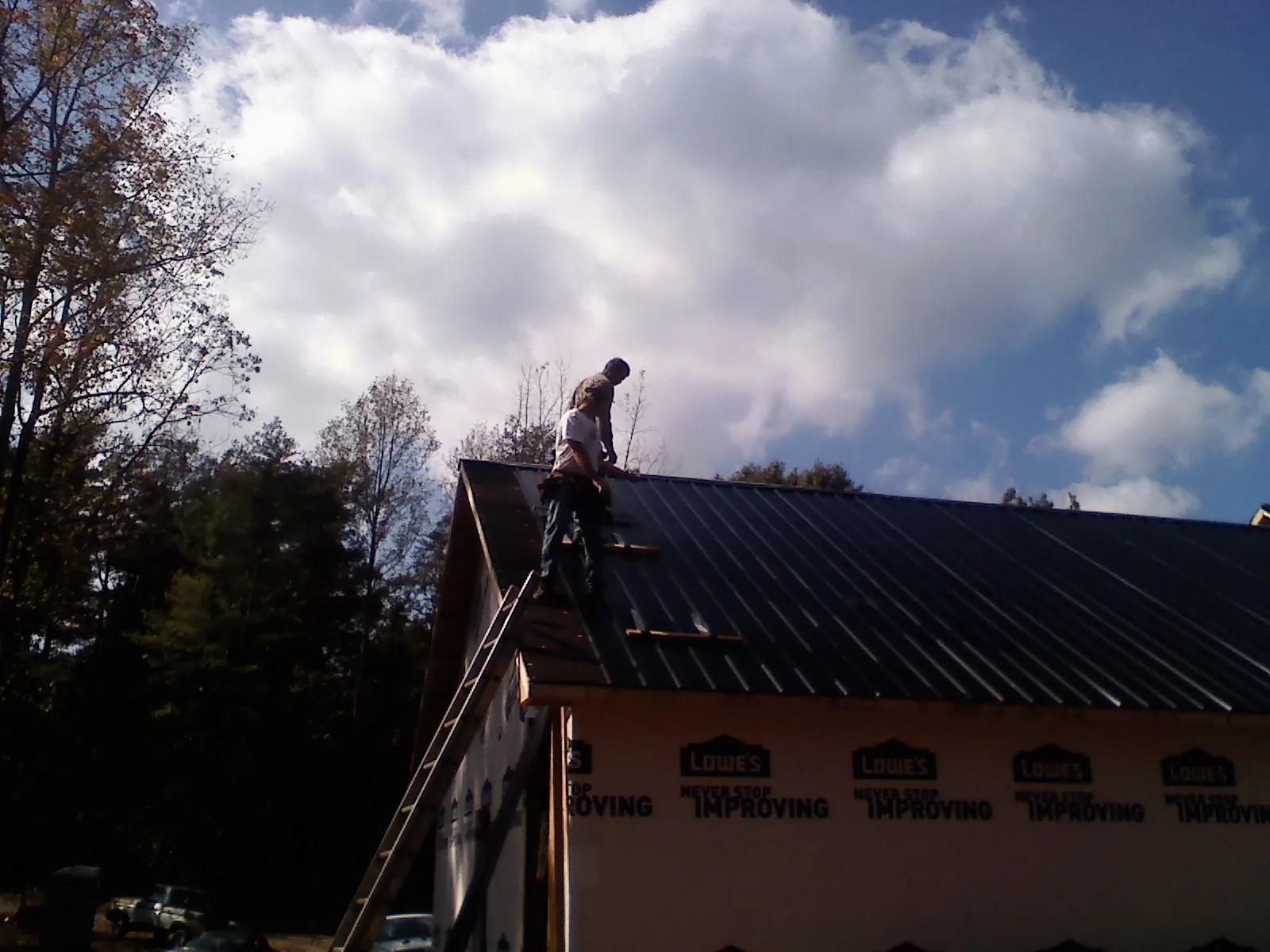 Roofer fastening dark metal panels high against a cloudy sky, from a Roof Inspection job in Glen Gardner