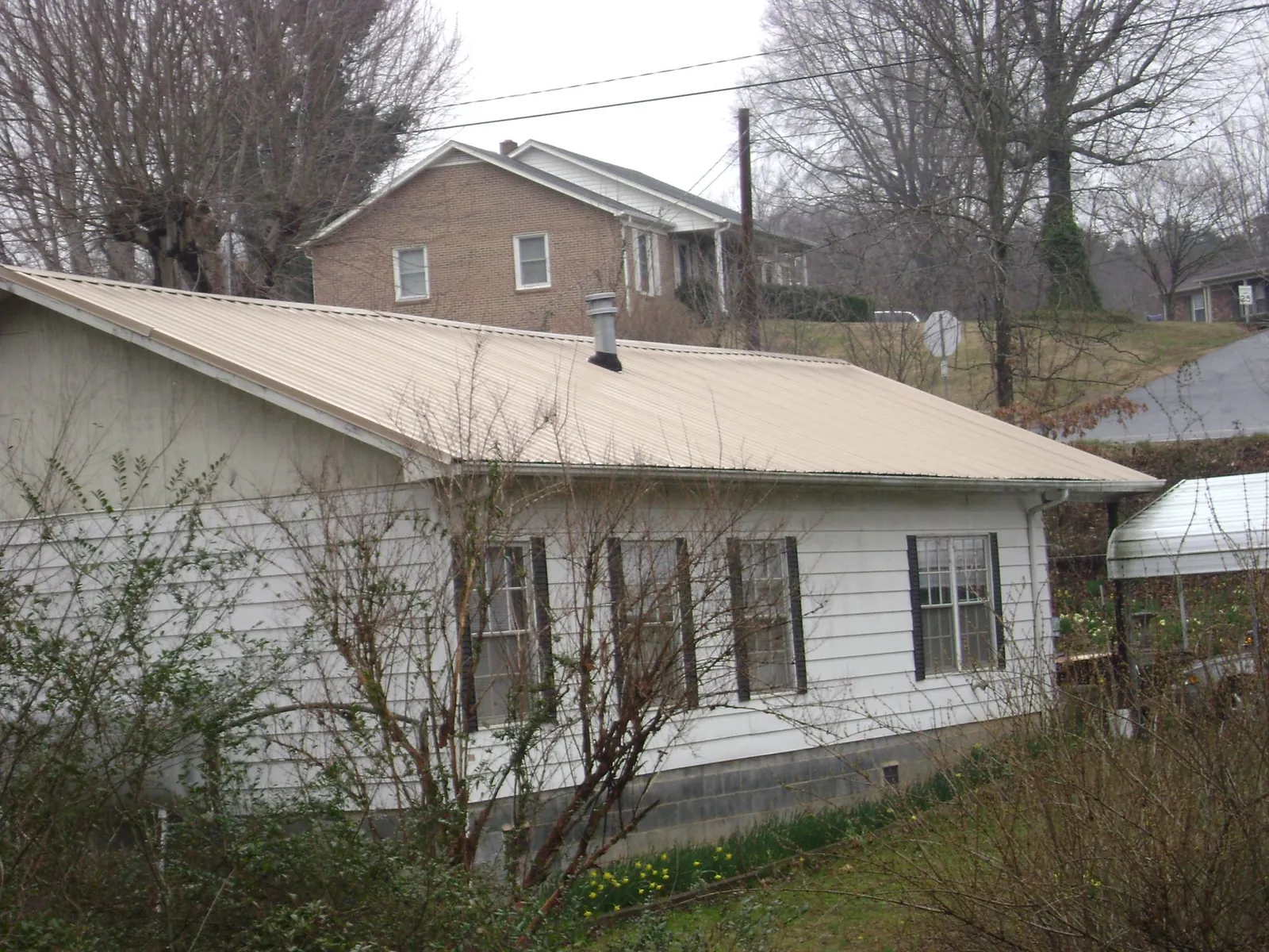 Tan metal roof on a white sided house set into a hillside — Commercial Roofing by Roofing Brothers in Glen Gardner